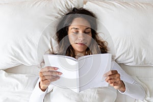 Young woman rest in cozy bed reading book at home