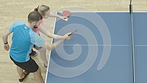 Top view of young Caucasian man and woman playing ping-pong. Female coach training sportive guy to play table tennis in