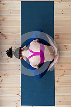 Top view of young Caucasian woman sitting in sleeping tortoise pose supta kurmasana on floor in studio