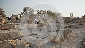 Top view of young caucasian woman wearing white summer hat and clothes walking on ruins of ancient temple and examining