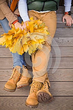 Top view on young couple holding bunches of yellow marple leaves and sitting on wooden stairs outdoors on autumn day