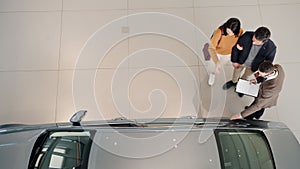 Top view of young couple purchasing automobile in car dealership talking to sales manager