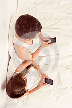 Top view of young couple sitting in bed with mobile phones