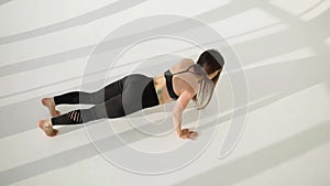 Top view of young european woman working out doing push-ups on a white sunny background.