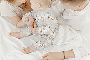 Top view of young family in white clothes sitting on white cotton bed linen with cute little blue-eyed baby infant.