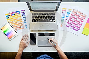 Top view of a young graphic designer working on a desktop computer and using some color swatches, top view