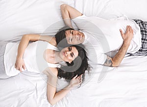 Top view of young happy millennial couple lying in bed