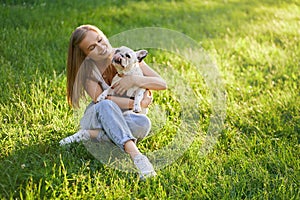 Smiling woman hugging french bulldog on grass.