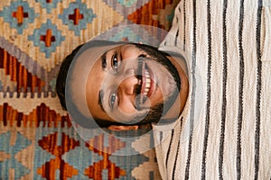 Top view of indian man smiling while laying on carpet at home