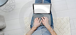 Top view of young man in casual clothes sitting on floor and working on his mockup laptop computer at home. Stay home and work