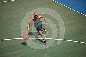Top view of young man, male basketball player playing basketball at street public stadium, sport court or palyground