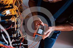 Top view of young man in uniform with measuring device that works with internet equipment and wires in server room