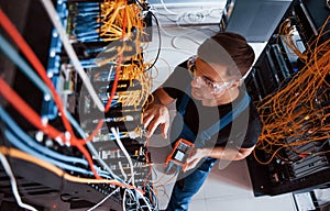 Top view of young man in uniform with measuring device that works with internet equipment and wires in server room