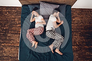 Top view. Young pregnant woman experiences contractions, lying next to sleeping adult man.