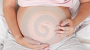 Top view of young pregnant woman stroking and touching gently her big belly. Concept of parenting and happy anticipation