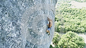 Top view young strong muscular tanned man rock climber climbing on a high vertical limestone cliff