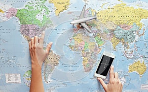 Top view of young tourist woman pointing her next travel destination using world map and mobile phone compass app