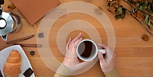 Top view of young woman holding coffee cup in comfortable workplace with office supplies