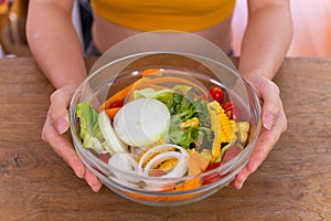 Top view of young woman holding salad bowl on wood table background