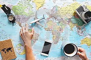 Top view of young woman planning her vacation using world map while drinking coffee - Tourist pointing the next travel destination