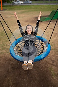 Top view of young woman swinging on hanging swing hands up smiling, concept of freedom, day off, remember childhood