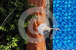 Top view of young woman in white dress and straw hat sitting near swimming pool. without face. Drone photo.Space for