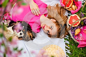 Top view young women on a picnic, lying on a blanket. A woman holds a dog. Next to the basket. Springtime