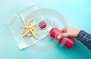 Top view of youngman squeezing a bottle sauce  ketchup  for dipping with french fried on blue color background photo