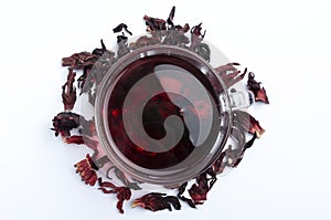 Top viewof glass cup of red hibiscus tea ad petals on the white background