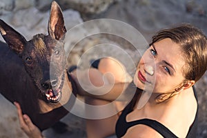 Top viw of Beautiful young girl and her dog breed xoloitzcuintle smiling on a stone beach summer