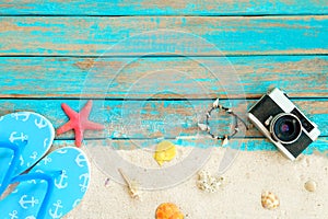 Top viwe of beach sand with slipper, starfish,shells, coral, retro camara and bracelet made of seashells on blue wooden backgroun photo