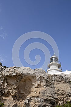 The top of a white lighthouse peeking over stone cliffs, Caballeria Lighthouse, Menorca, Balearic Islands photo
