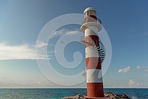 Top of a white-red lighthouse against a blue sky with an airplane.