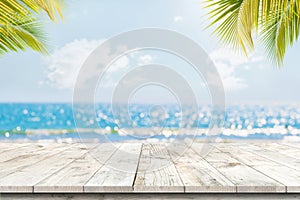 Top of wood table with seascape and palm leaves, blur bokeh light of calm sea and sky at tropical beach background