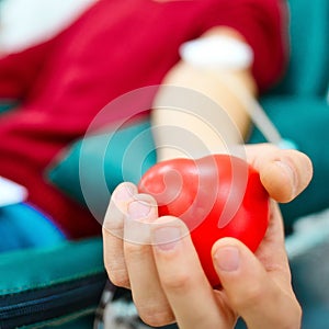 Topic of donation. Man donates blood in hospital. Man's hand squeezes rubber heart. Close-up. Donor sits in chair.