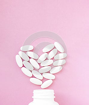 Topic of treatment for covid-19, White pills in heart shape with bottle on pink background. Copy space for text