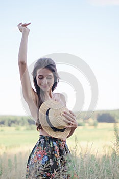 topless brunette woman covering her breasts with straw hat in the field