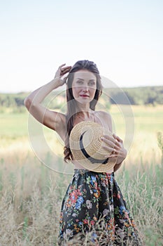 topless brunette woman covering her breasts with straw hat in the field