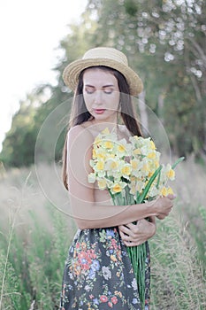 topless brunette woman in straw hat covering her breasts with flowers in the field