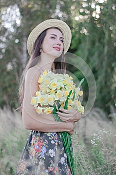topless brunette woman in straw hat covering her breasts with flowers in the field