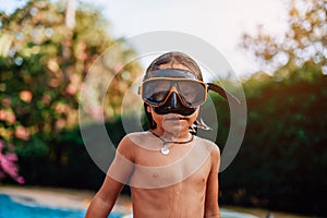 Topless kid with goggles pose around swimming pool in sunny day