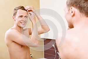 Topless man fixing his hair in bathroom