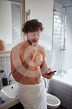 Topless man texting while brushing teeth