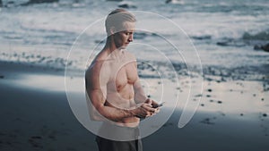 Topless young sportsman uses his smartphone at the sea shore.