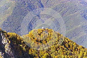 The tops of the mountains covered with snow. The slopes are thickets of yellow and green trees.