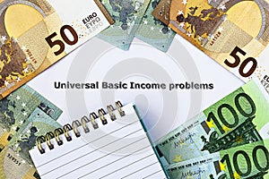 Topview photo on Universal Basic Income theme. The words Universal Basic Income problems, on paper, surrounded by euro banknotes