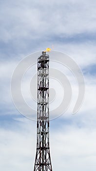 A torch of fire burns atop an oil derrick, refining an oil and gas facility.