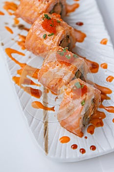 Torched Salmon Maki Sushi with Shrimp Tempura, Avocado and Cheese inside. Topping with Sauce, Ebiko Shrimp Egg and Scallion