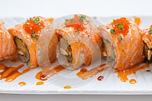 Torched Salmon Maki Sushi with Shrimp Tempura, Avocado and Cheese inside. Topping with Sauce, Ebiko Shrimp Egg and Scallion