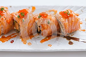 Torched Salmon Maki Sushi with Shrimp Tempura, Avocado and Cheese inside. Topping with Sauce, Ebiko Shrimp Egg and Scallion